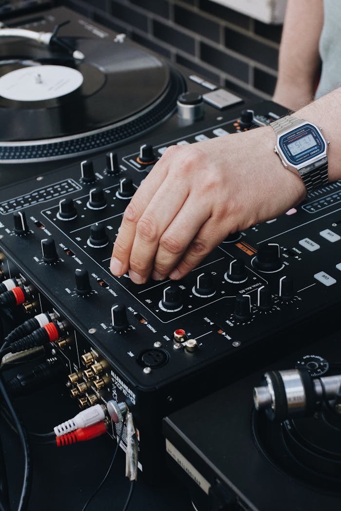DJ adjusting controls on a music mixer, showcasing a close-up of the device with a turntable in view.