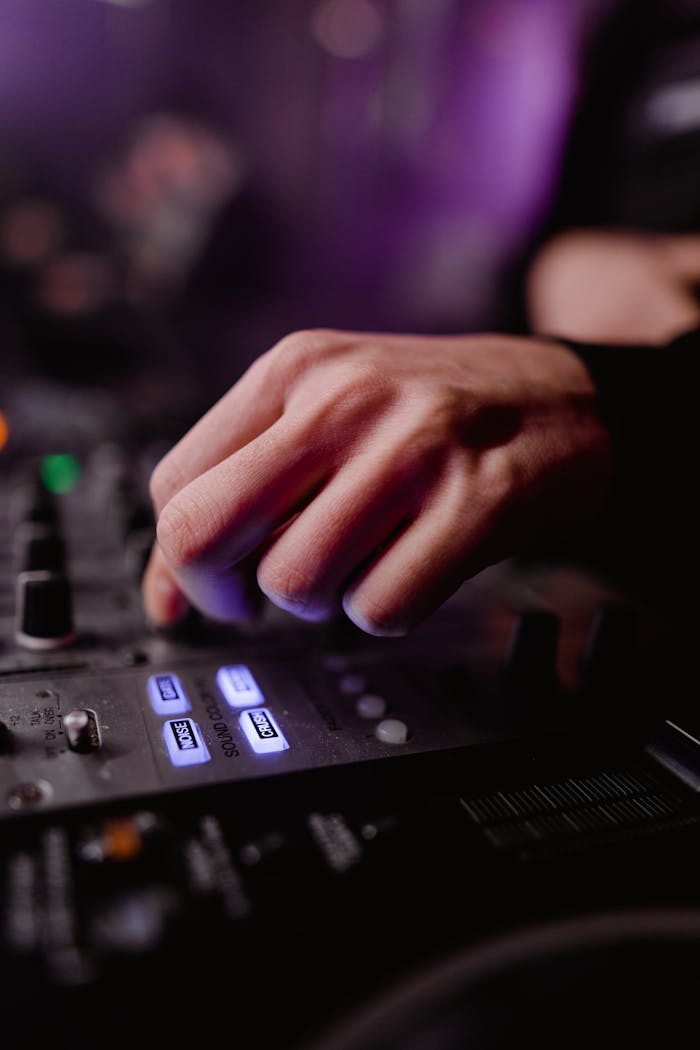 Close-up of a DJ's hand adjusting audio mixer controls under vibrant nightclub lights.