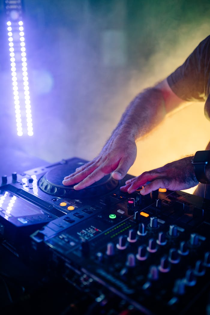 Dynamic DJ performance with vibrant lighting, highlighting hands mixing music on a professional DJ console.